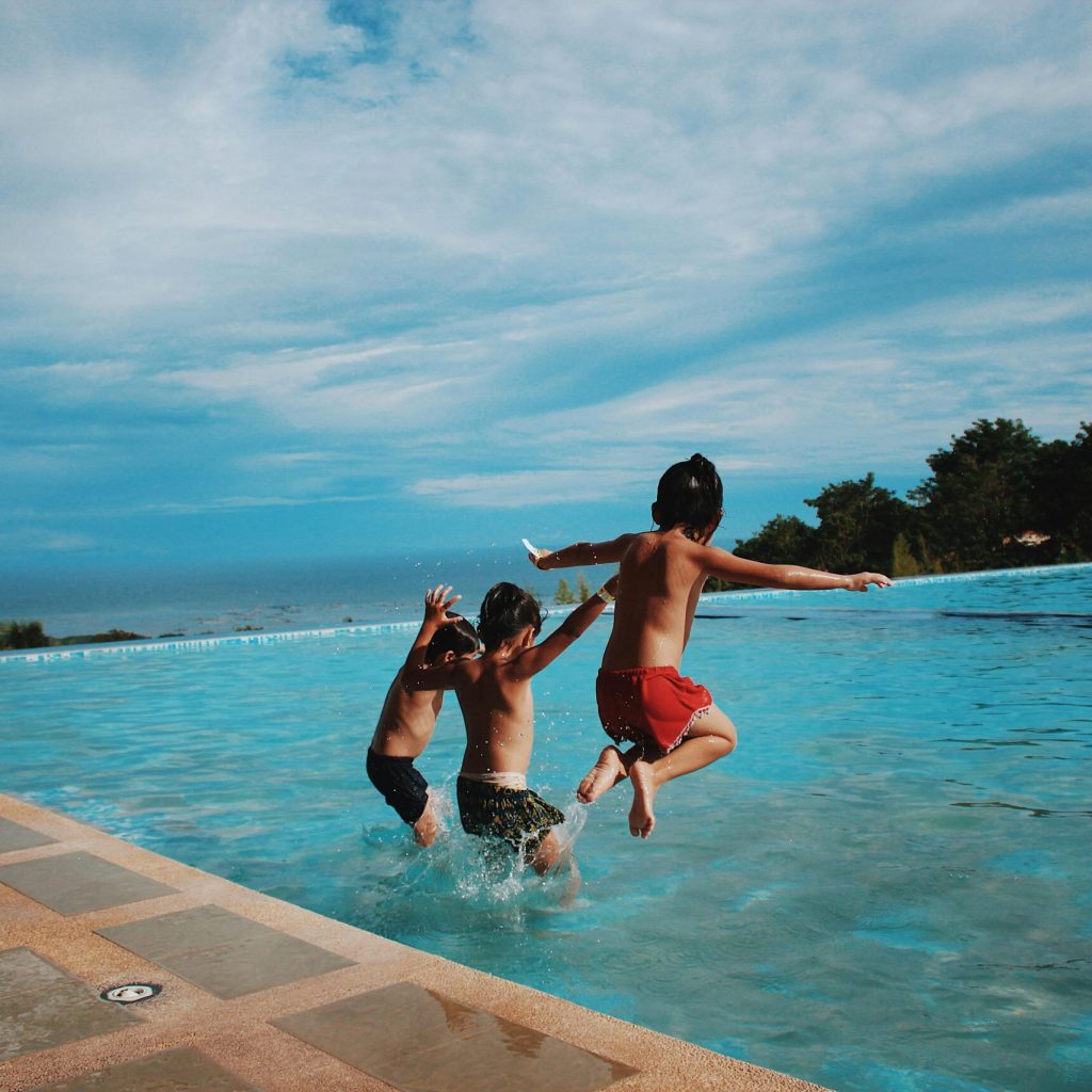 Two children joyfully jump into a pool on a sunny day, embodying excitement and summer vibes.